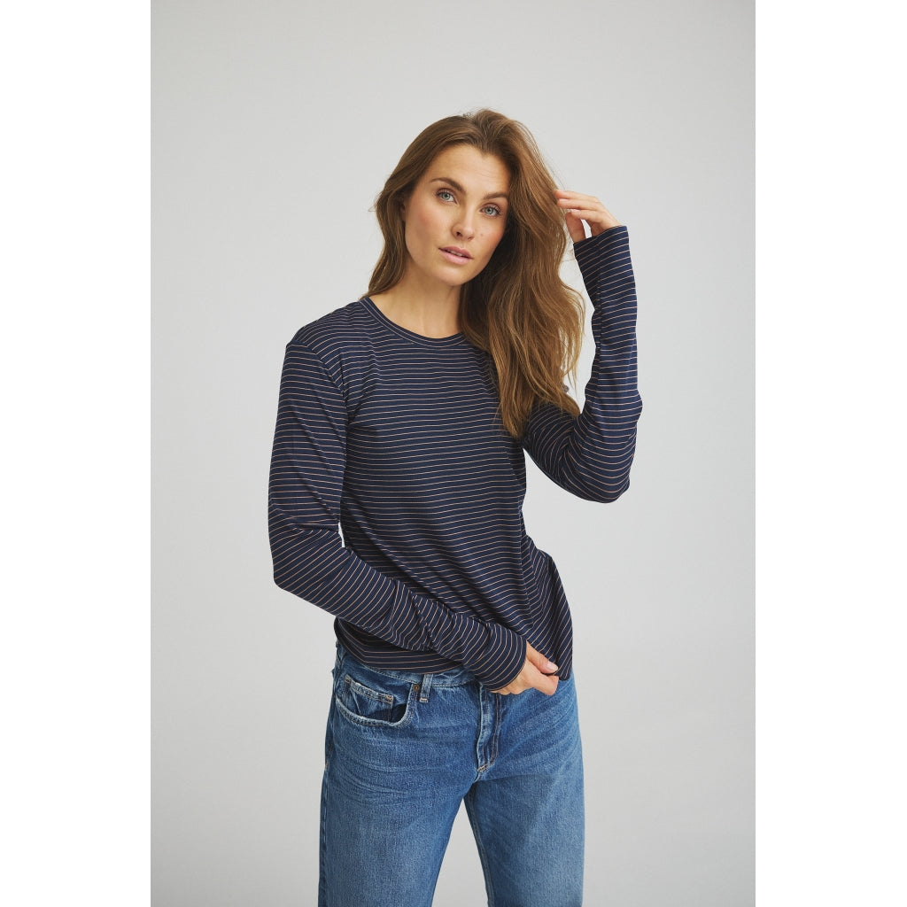 Kvinde iført en Luxzuz 156421 – Segberg Mørkeblå langærmet skjorte med tynde hvide vandrette striber og blå jeans.