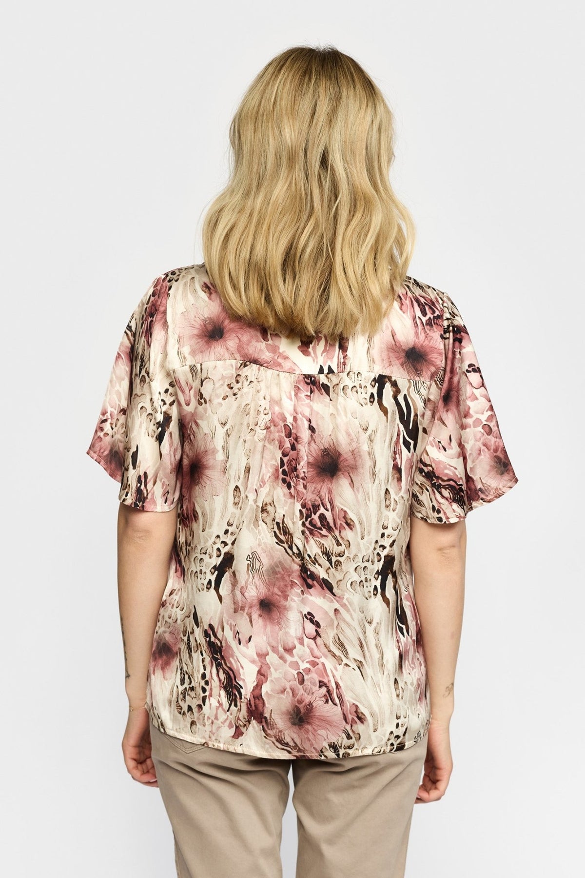 En blond person iført en 2-Biz Amora Rosa-mønstret bluse og beige bukser, set bagfra.