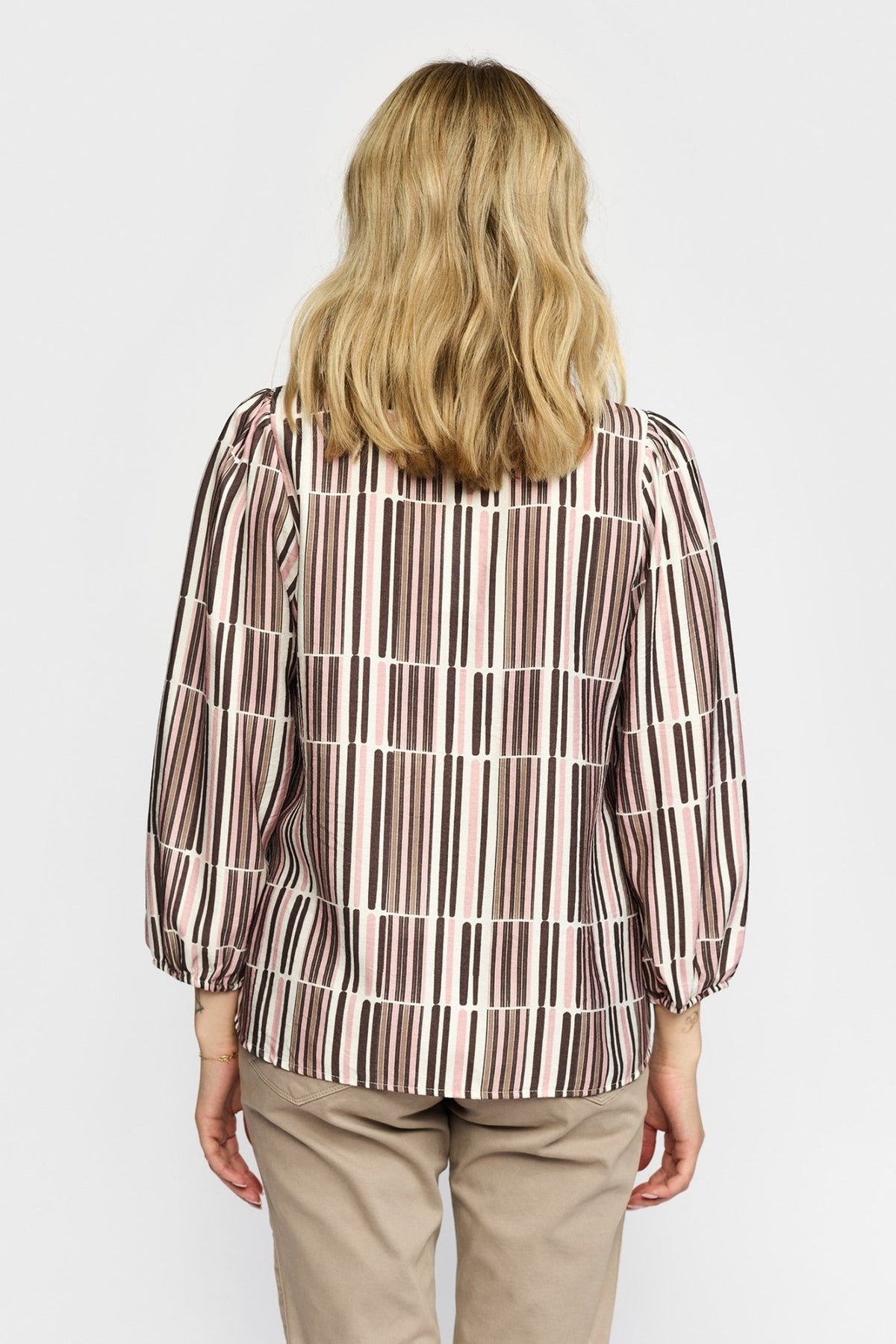 En blondine er iført en 2-Biz Esmara Rosa-mønstret bluse og beige bukser, fotograferet set bagfra.