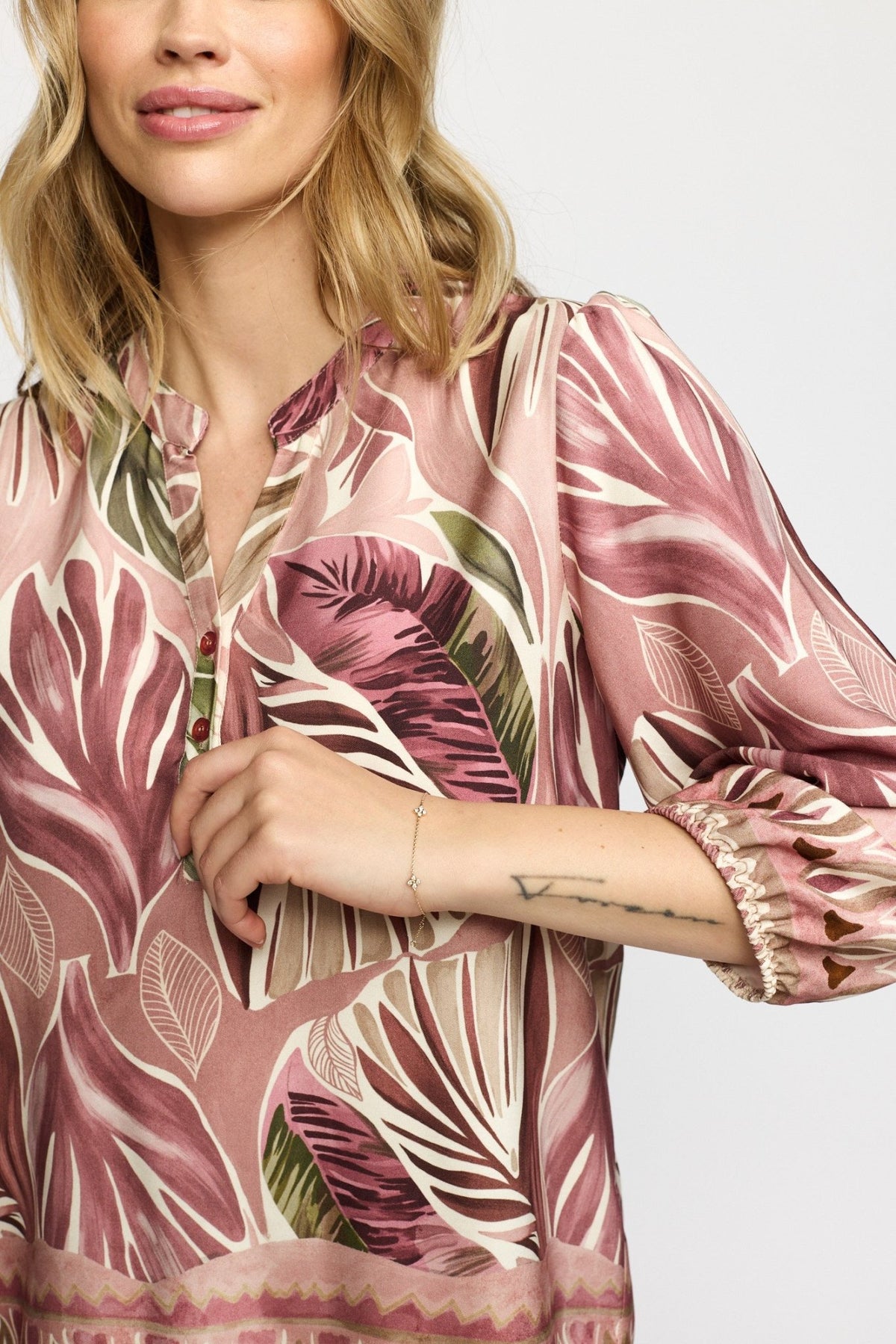 En kvinde iført en Ellen Gammelrosa-bluse fra 2-Biz med lyserødt og beige mønster, der står foran en ensfarvet lys baggrund.