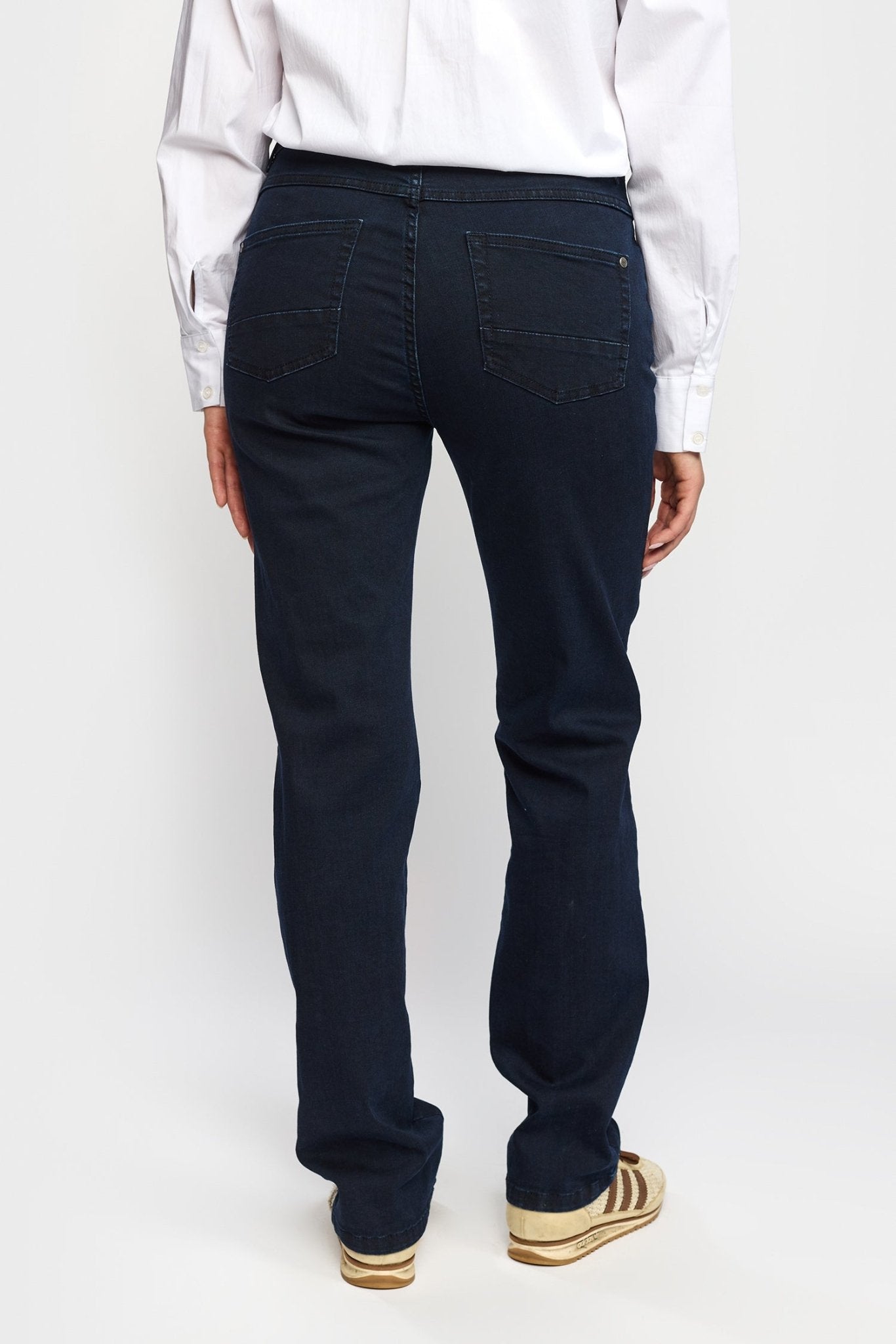 En person iført 2-Biz Bekket Mørk-jeans, en hvid skjorte med knapper og beige sneakers; set bagfra.