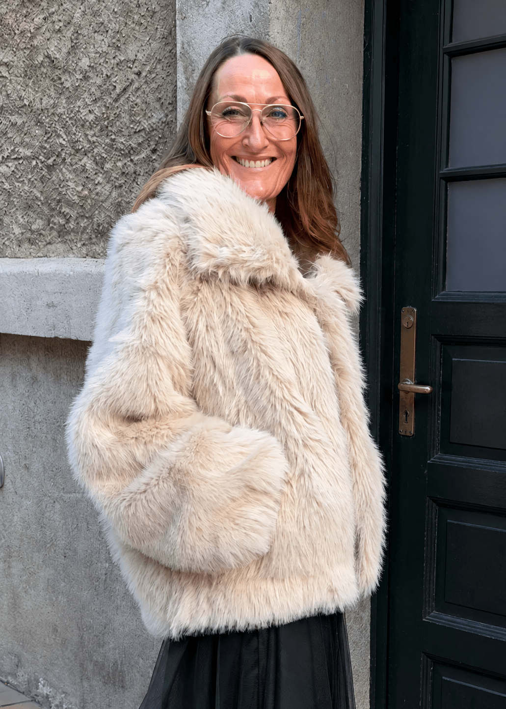 En smilende kvinde iført en beige 155917 | 2NDDAY - 2NDFritz Sand-jakke i imiteret pels og store solbriller.
