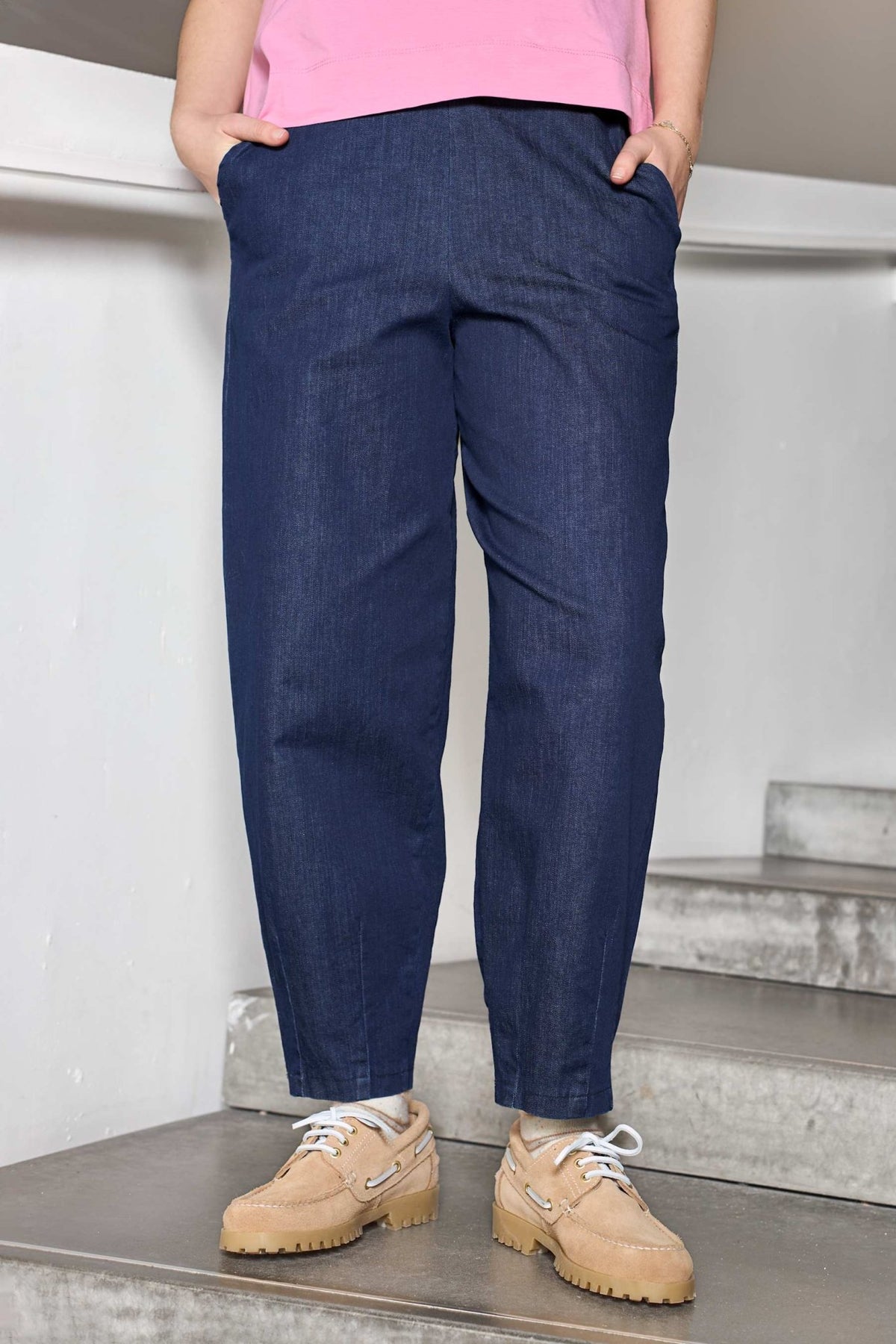 En person iført sort Denice Mørk-denim og en lyserød skjorte står på en betontrappe med hænderne i lommerne.