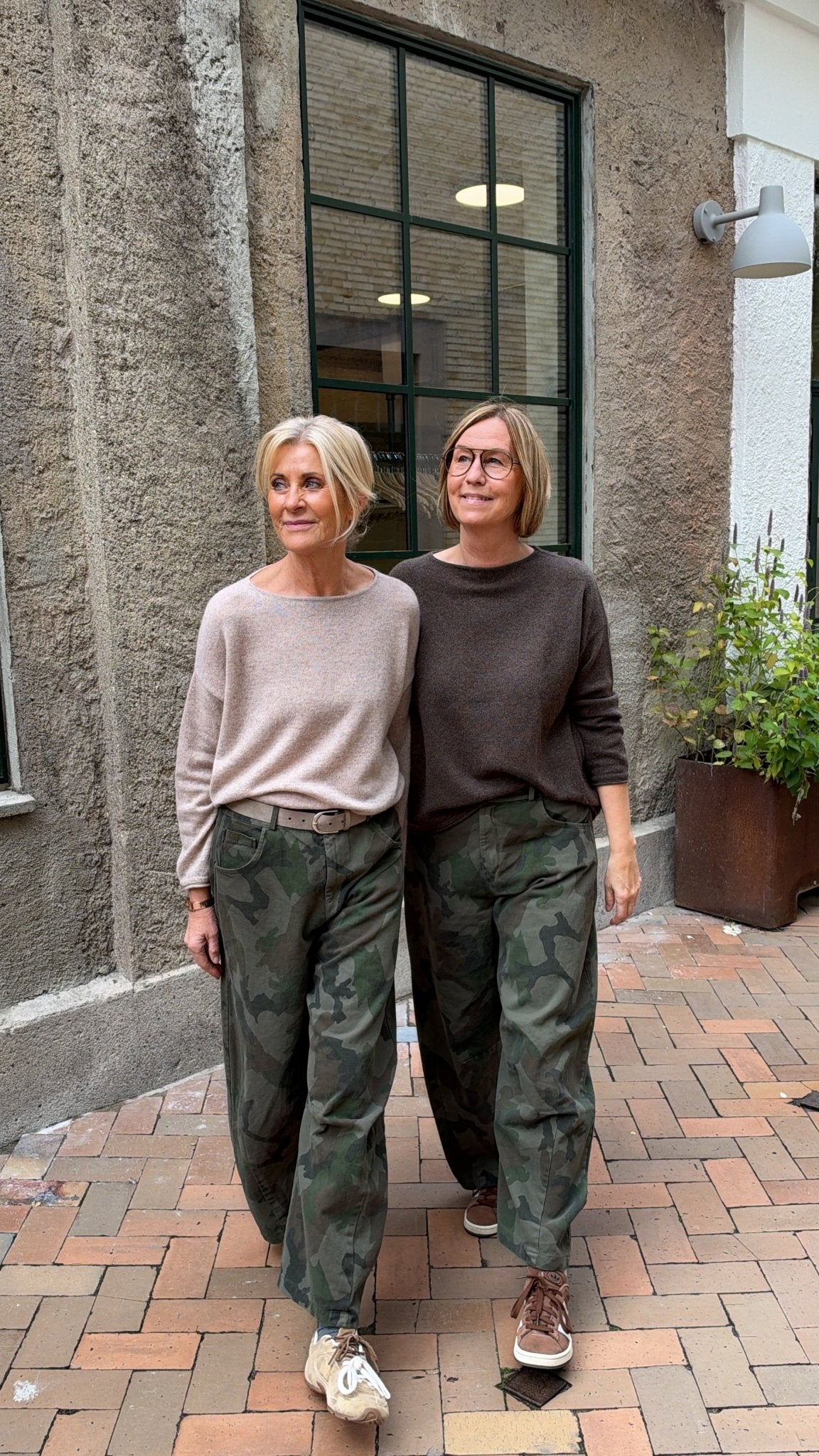 To kvinder iført beige trøjer og 156444 | Cabana Living – Wild Balo Army-mønstrede camouflagebukser går side om side.