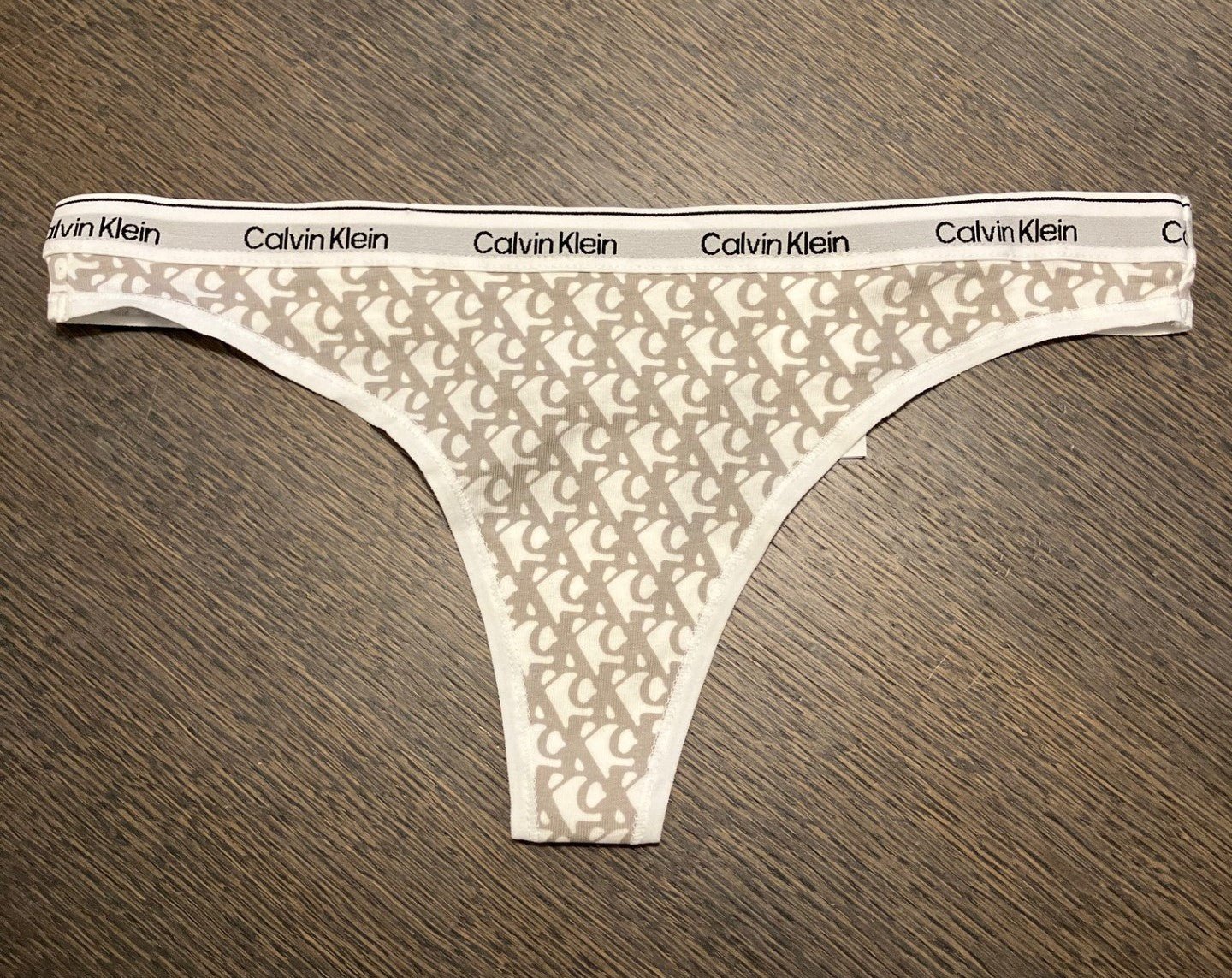 Calvin Klein – 3 FOR 399,- mønstret G-streng med hvidt logo-bånd, der ligger fladt på træoverfladen.
