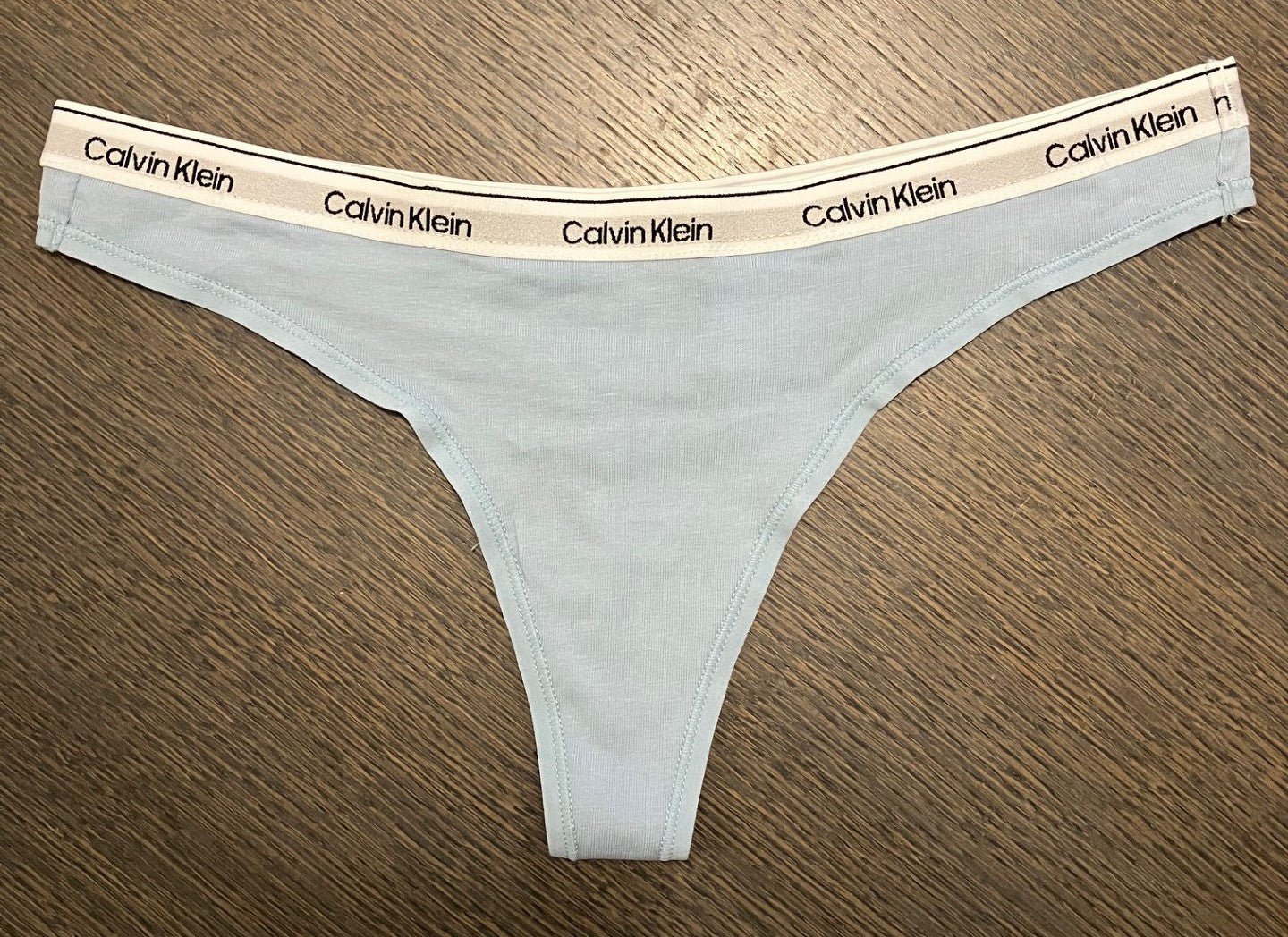 Lyseblå Calvin Klein 150132 G-streng med logo-foring, lagt fladt på mørkt træ.