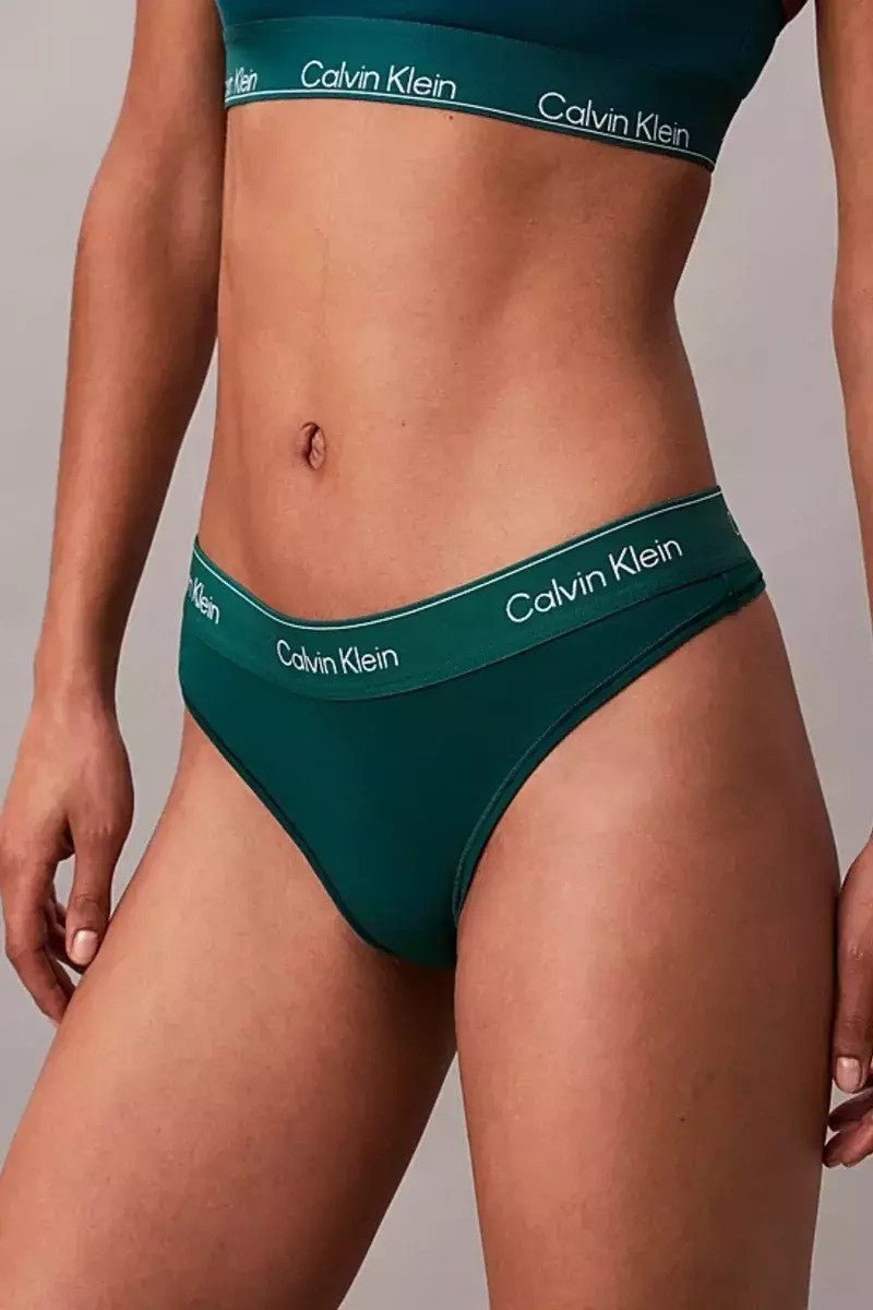 Person iført Calvin Klein – QF8518 Mørkegrøn G-streng, lav talje, logoet ses på linningen.