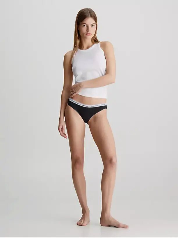 En kvinde poserer i en hvid tanktop og Calvin Klein 3 FOR 399,- Sort undertøj med hvid kant.
