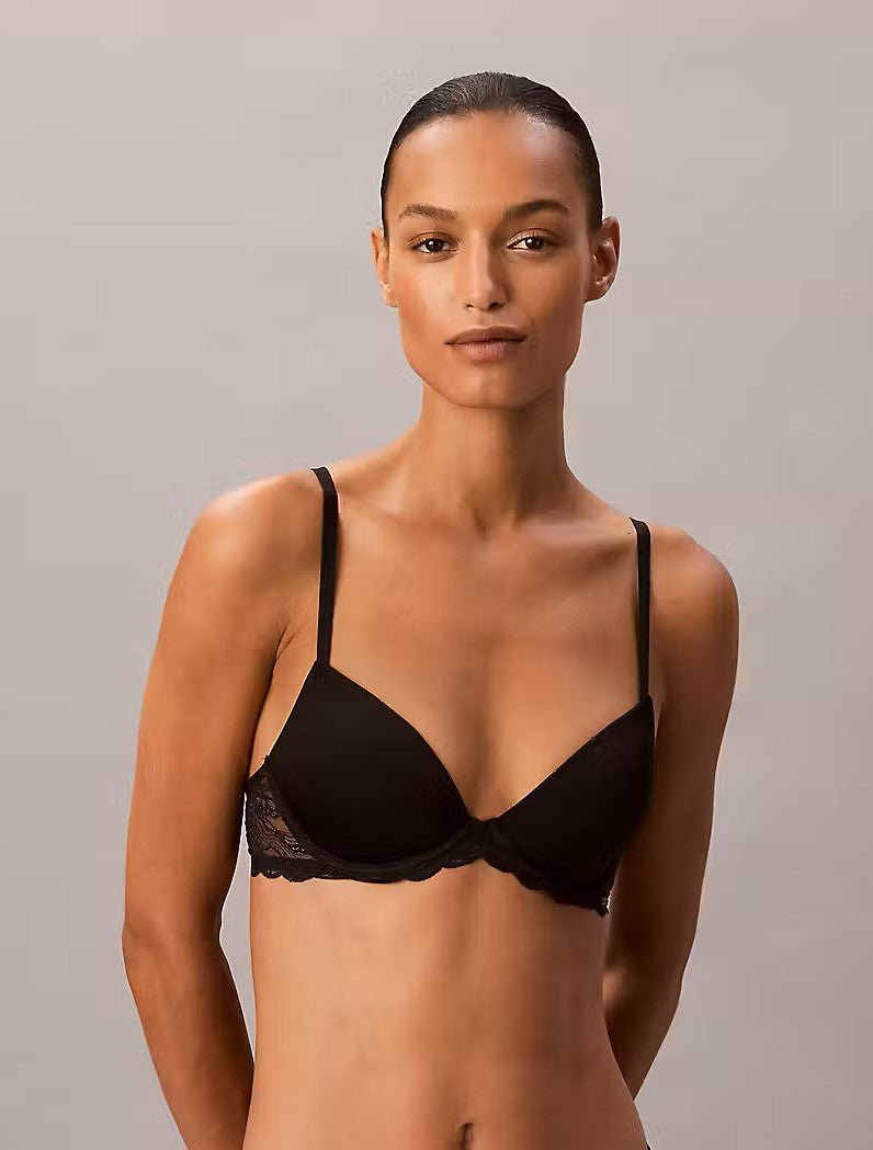 En kvinde iført Calvin Klein Sensitive Seductive Lace-undertøj, der poserer foran en ensfarvet baggrund og ser ind i kameraet.