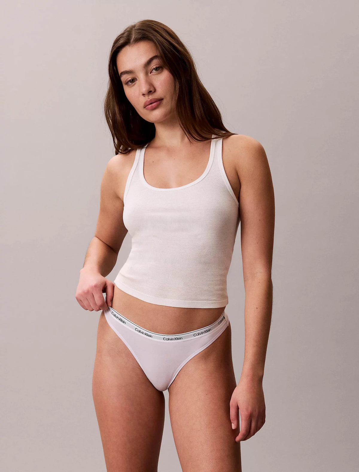 Kvinde i hvid tanktop og en Lyselilla G-streng fra Calvin Klein 3 for 399,- på en ensfarvet lysegrå baggrund.