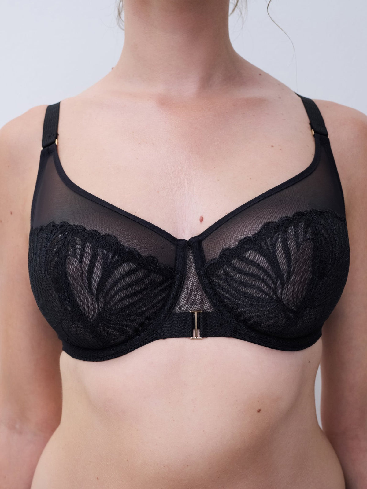 Modellen bærer Chantelle Legend Black Sort, en gennemsigtig mesh-bh med blonder og blomsterdetaljer, som ses fra skuldrene til maven.