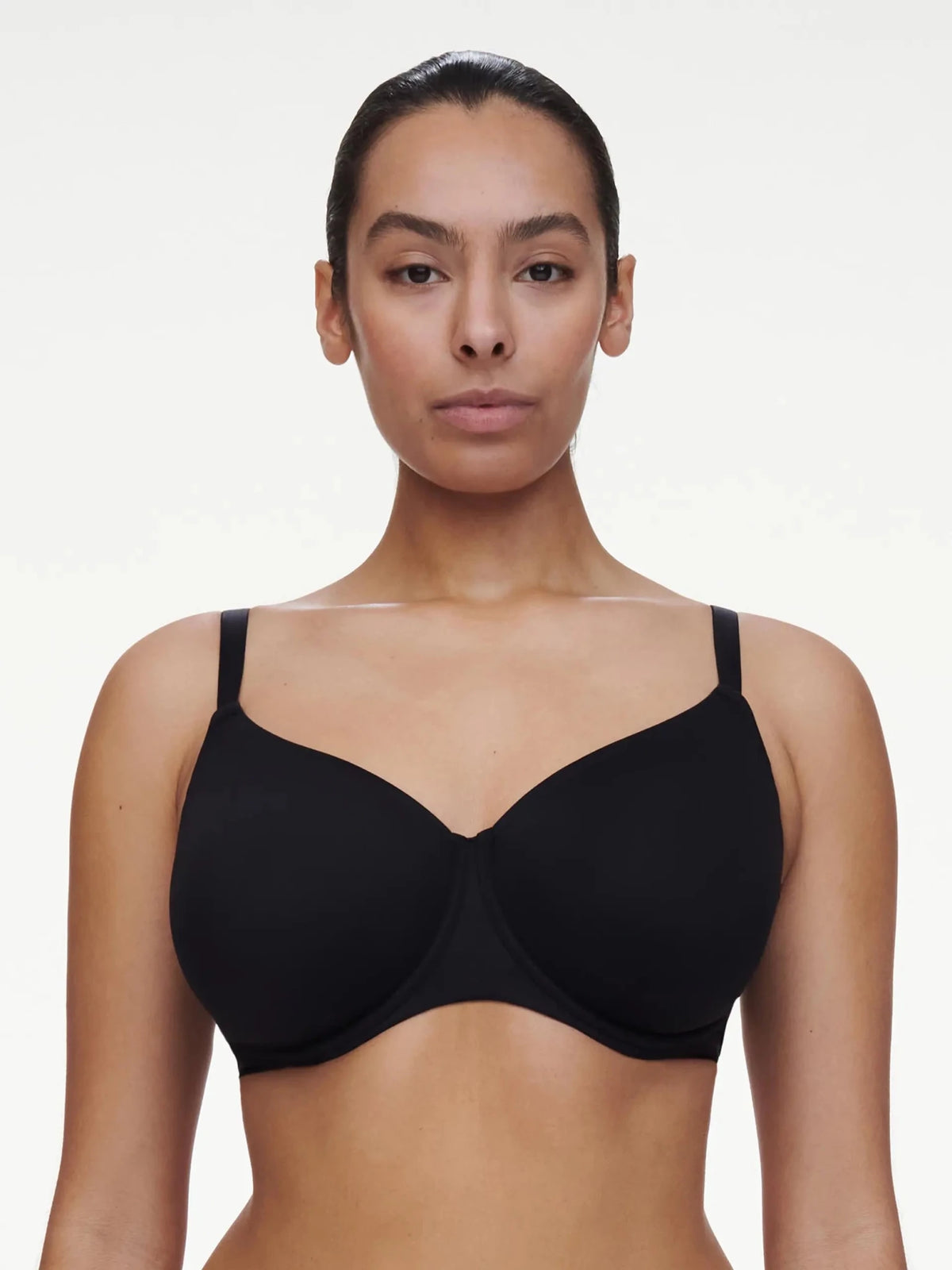 En kvinde bærer en Chantelle EasyFeel Easy Bliss 011 Sort bh med fulde skåle og står med forsiden mod et ensfarvet hvidt baggrund.