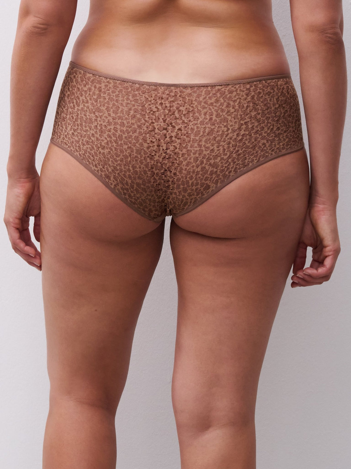 Billede af en person set fra taljen og ned, iført Chantelle EasyFeel – Norah Wild Brown Brun hipster, stående ved en lys væg.