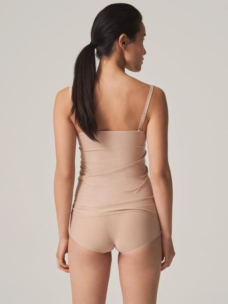En kvinde står med ryggen til kameraet og har en Chantelle Seamless Soft Stretch-camisole i farven Sand på samt matchende undertøj.