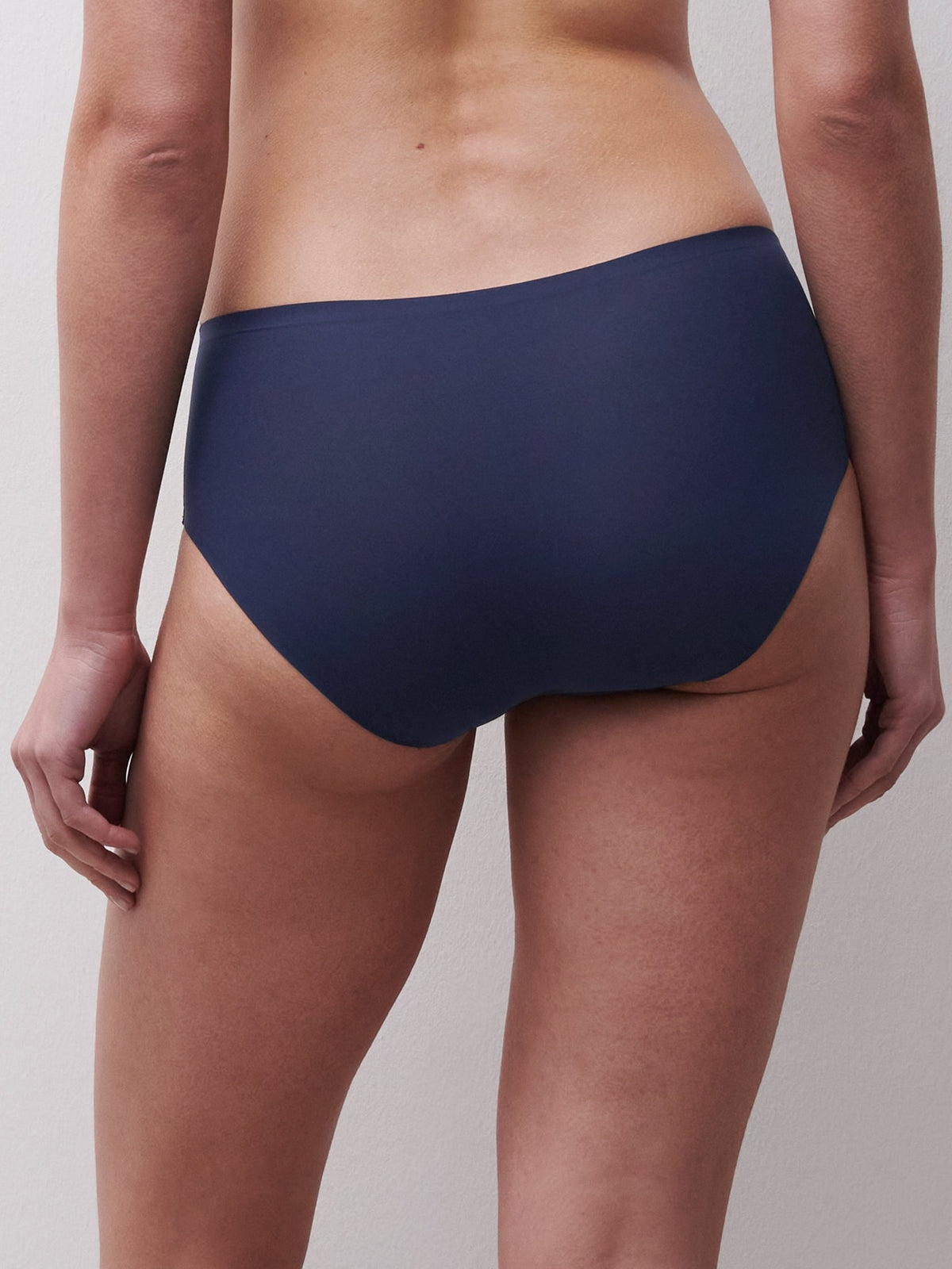 En person, der står med ryggen til kameraet, har Chantelle Seamless - Soft stretch hipster i mørkeblå på sig foran en lys baggrund.