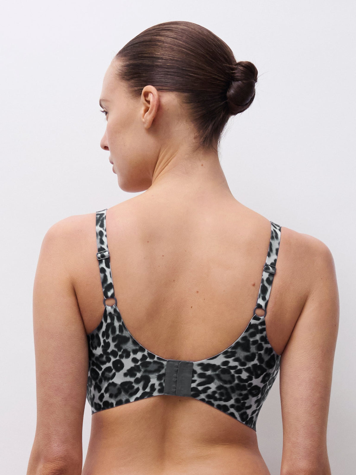 En kvinde med håret sat op viser modellen Chantelle Seamless 152391 Soft Stretch Power i gråt mønster, set bagfra, på ensfarvet baggrund.