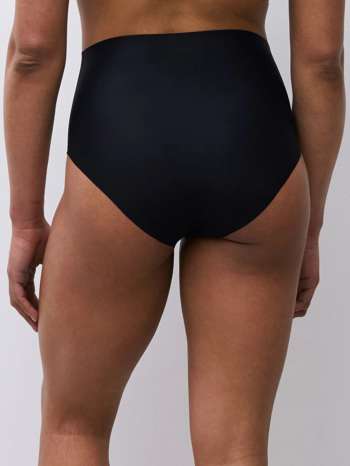Model iført Chantelle Seamless 155788 Defi Sort maxi-trusser med høj talje, set bagfra, på en ensfarvet lys baggrund.