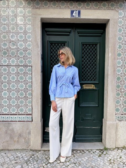 En kvinde i en blå bluse og off-white bukser fra Copenhagen Muse Tailor står ved en mørkegrøn dør med nummeret 41.