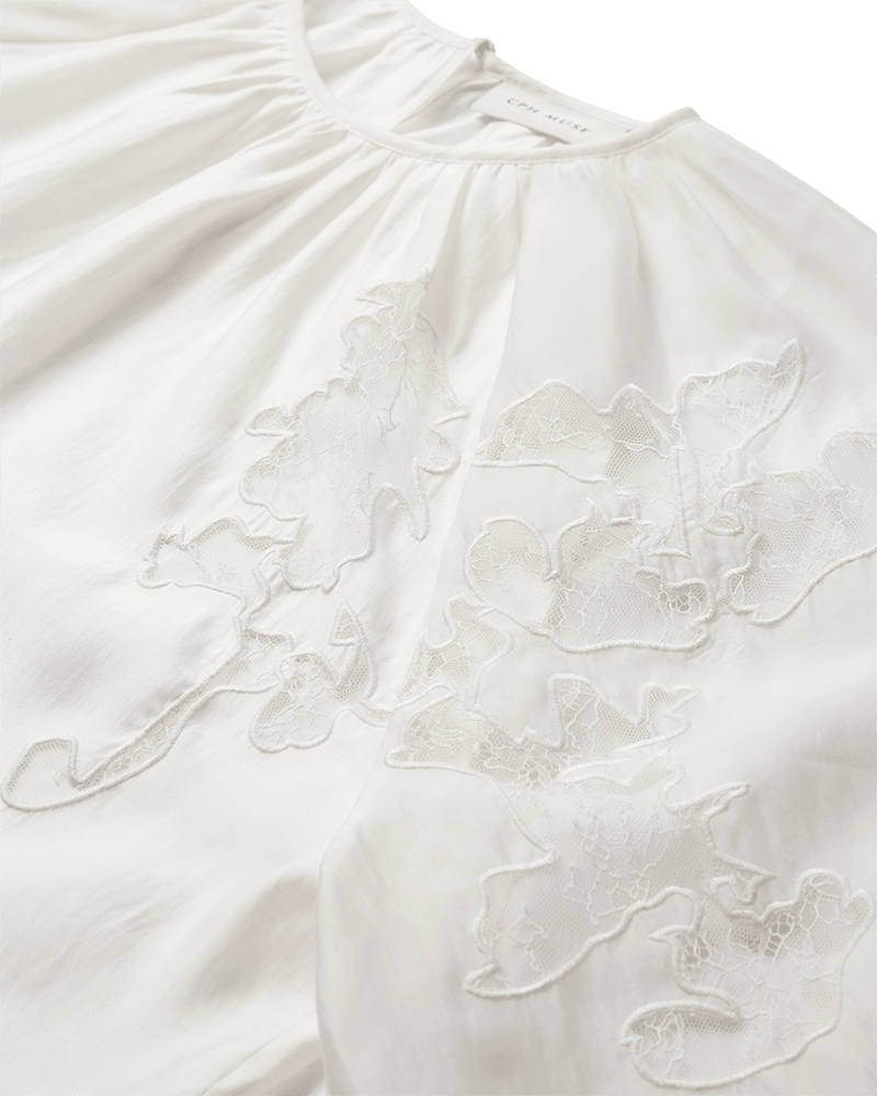 Copenhagen Muse Molly-bluse i offwhite med rund hals, blomsterbroderi og ballonærmer, vist udbredt.