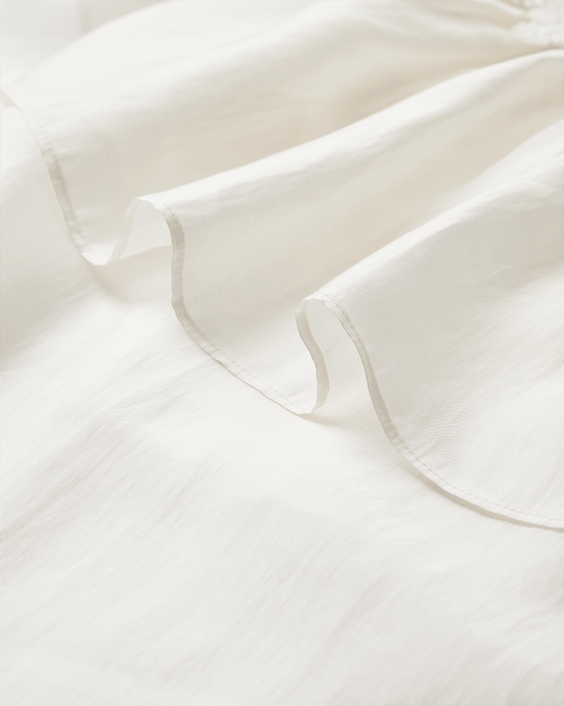Nærbillede af blusen »Molly« fra Copenhagen Muse i offwhite, med bløde folder og en let, halvgennemsigtig tekstur.