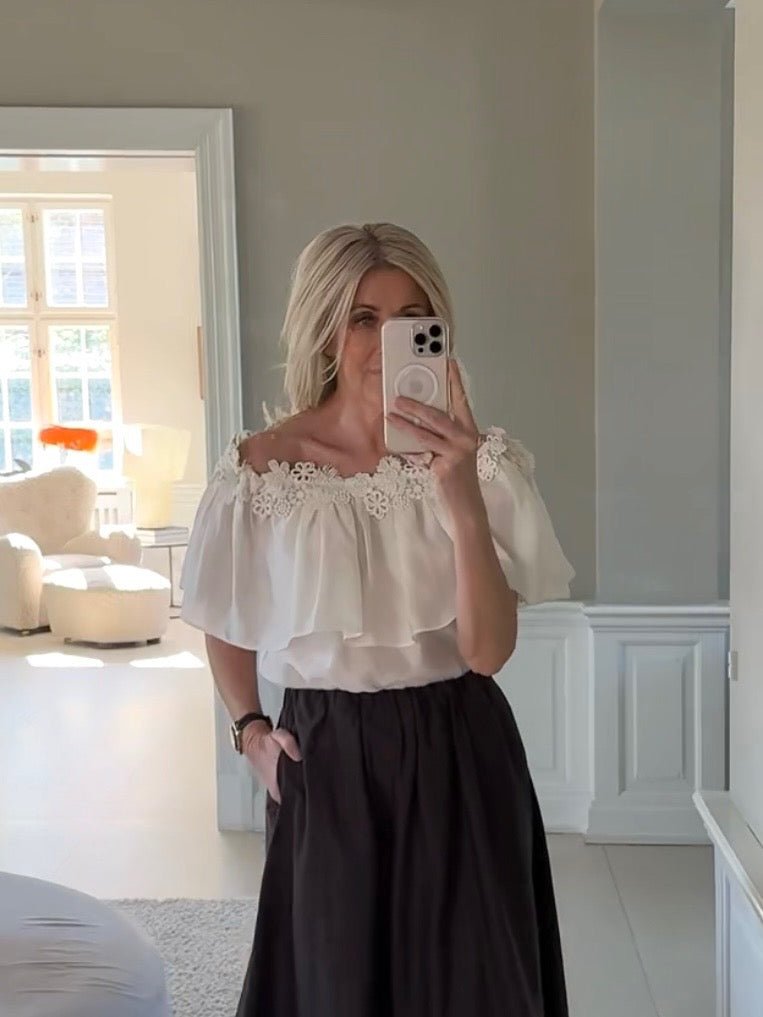Kvinde iført en bluse fra Copenhagen Muse Molly i off-white og et sort nederdel – en elegant og moderne stil fra Copenhagen Muse.