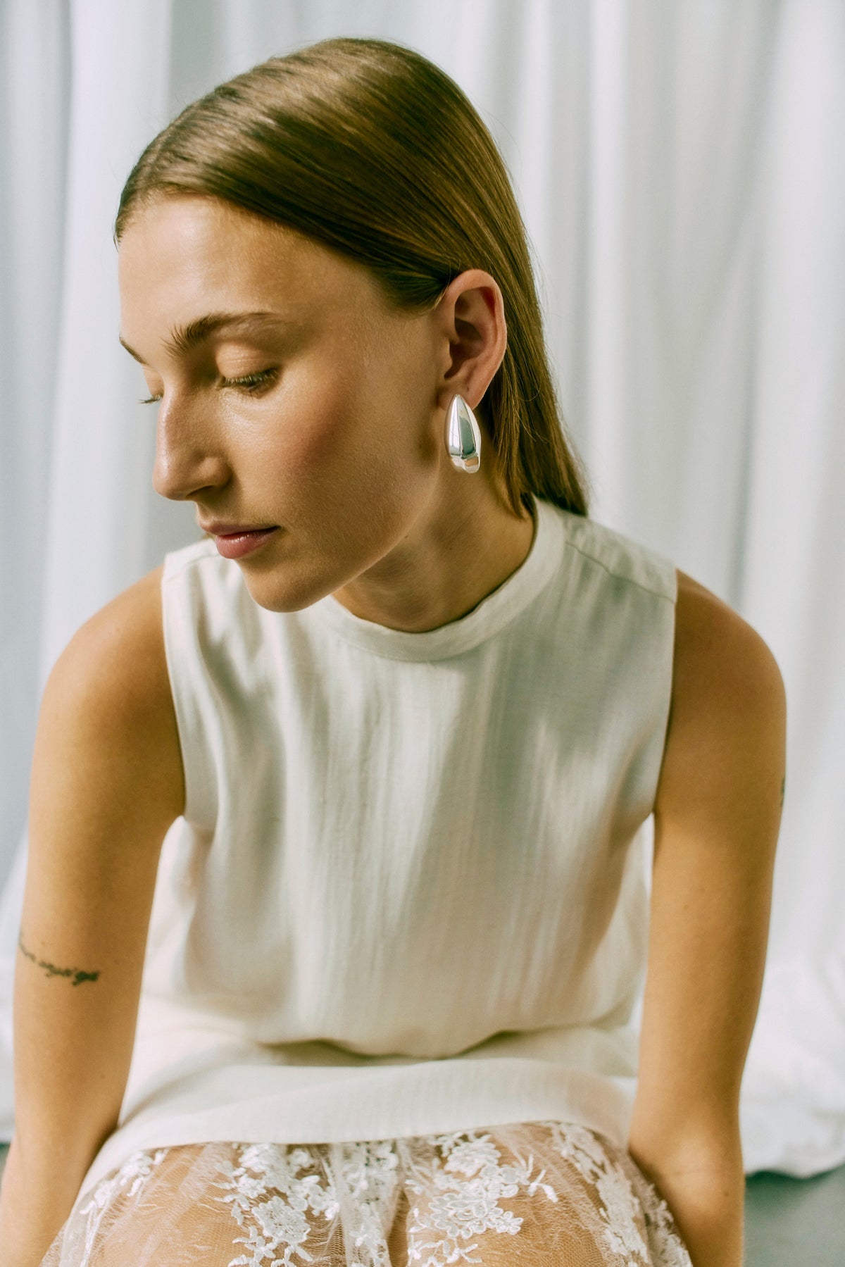Kvinde i København iført en Muse Tenley Off White-top, med glat lysebrunt hår og sølvøreringe – en elegant og moderne stil.