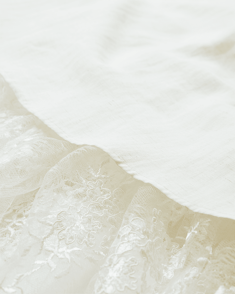 Nærbillede af Copenhagen Muse Tenley Off White: detaljerede blomstermønstre i blonder ved siden af glat, ensfarvet stof.