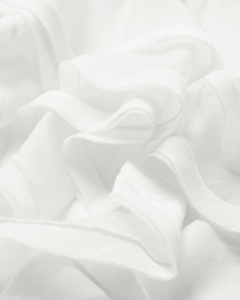 Et nærbillede af de gennemsigtige, hvide folder fremhæver elegancen i Copenhagen Muses »Tilly Off White«-bluse med én skulder.