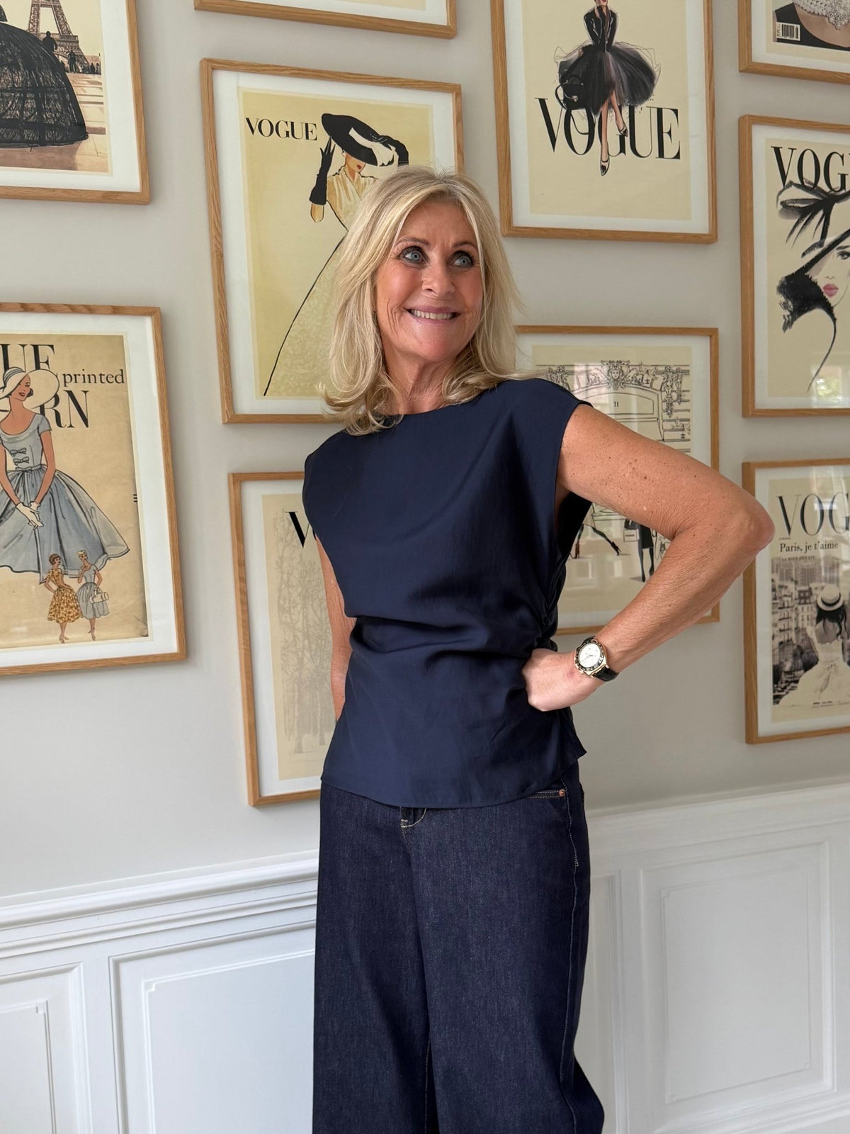 En kvinde iført blusen »Copenhagen Muse Molly Marine« og jeans står foran indrammede Vogue-forsider.