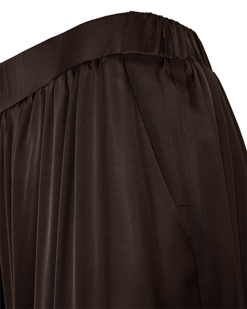 Nærbillede af brune, plisserede Freequent Dova Kaffe-bukser i satin med elastisk talje og sidelomme på hvid baggrund.