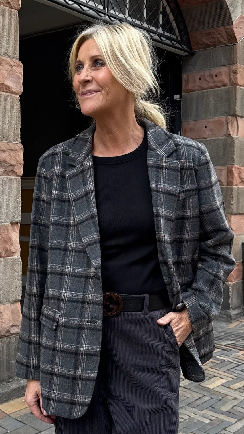 En blond kvinde med hestehale går udenfor iført en Freequent Zango Mørkegrå blazer, en sort skjorte og mørke bukser.