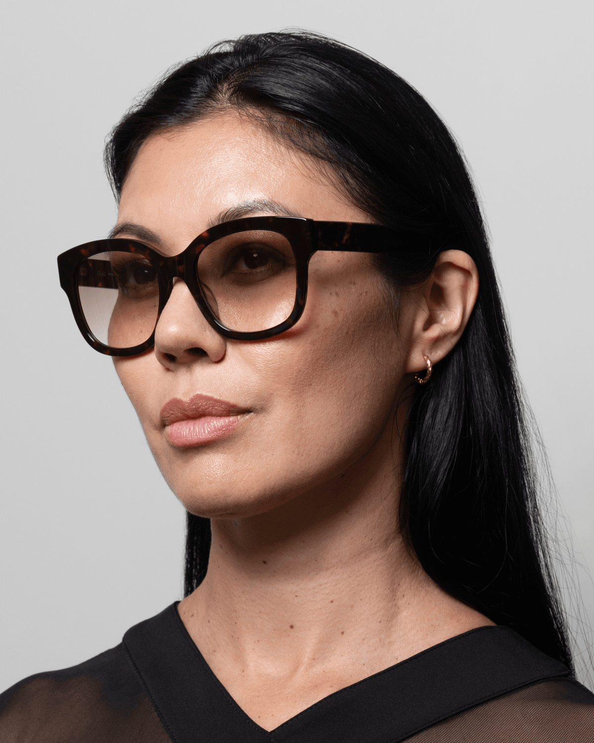 Kvinde med langt sort hår i GLAS – Kate Brun-mønsteret fra GLAS, iført en sort top, der kigger let til siden.