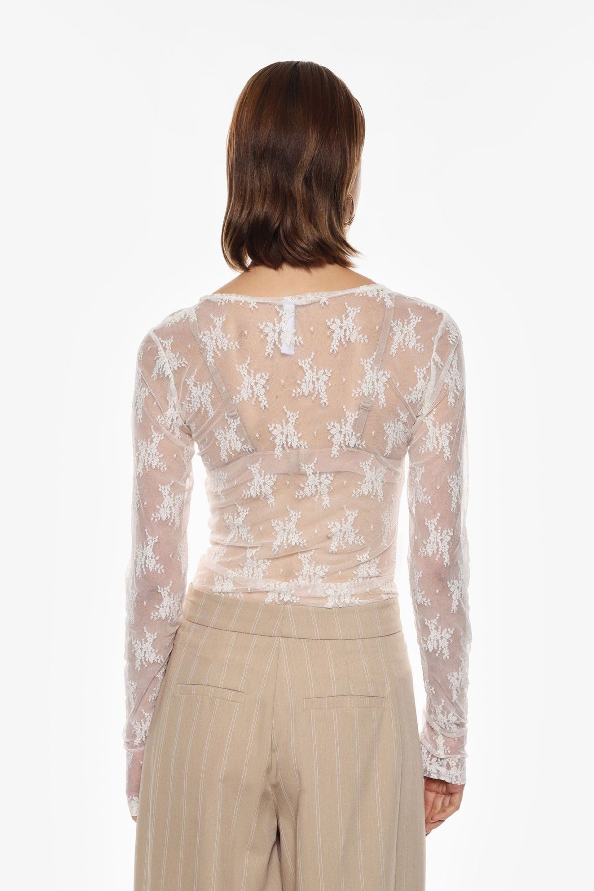 Personen står med ryggen til kameraet i Imperial - TW91: Offwhite bluse, beige bukser med tynde striber, på en ensfarvet hvid baggrund.