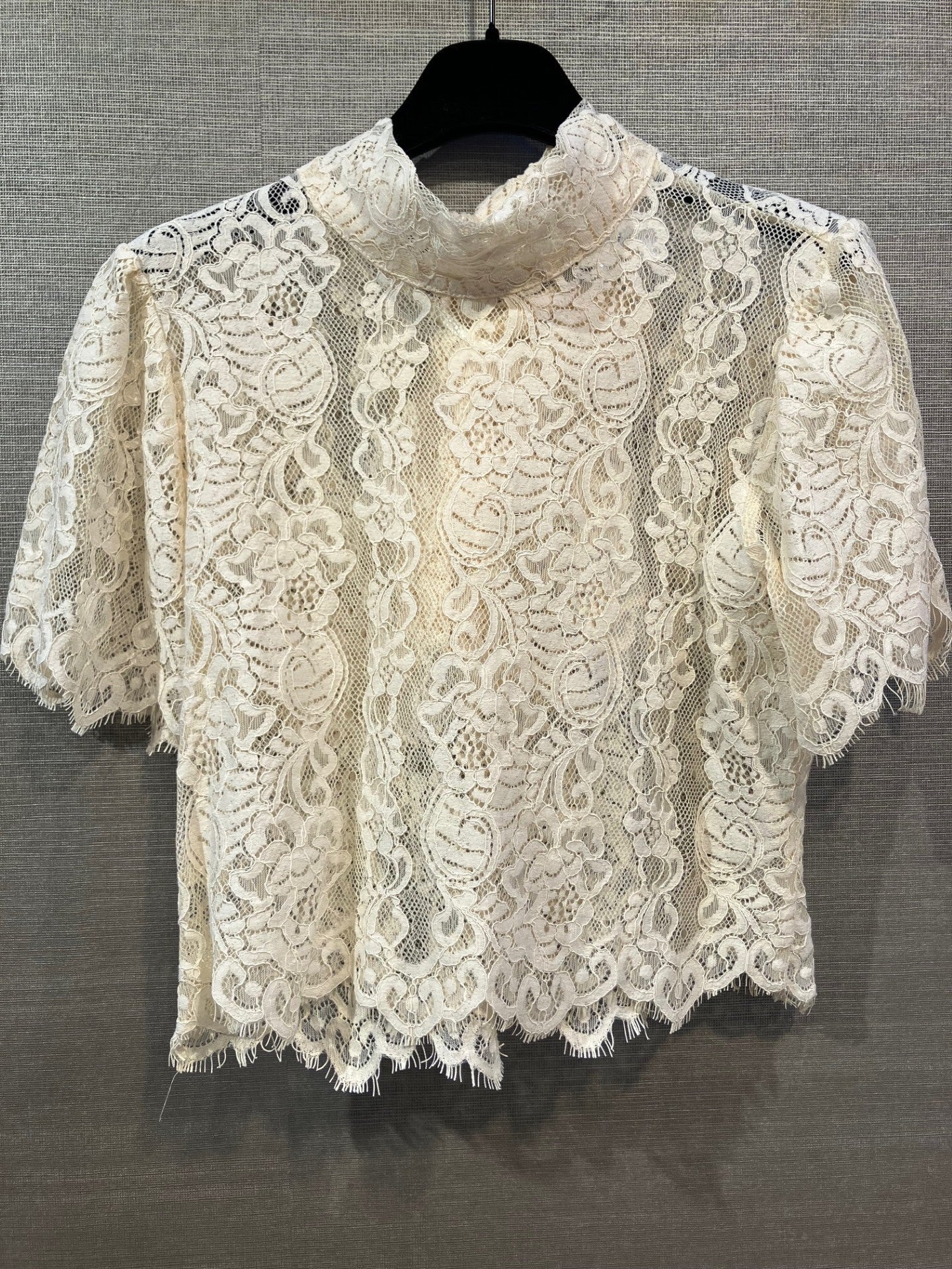 Imperial 154149 RIT8 kortærmet bluse med blonder i offwhite, vist på en bøjle foran en grå, struktureret baggrund.