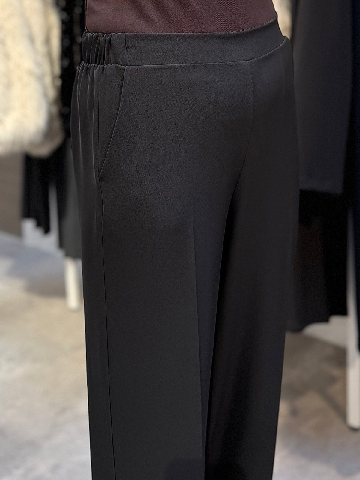 Nærbillede af en person iført Imperial P4L0 Easy Bukser Kaffe, vist fra taljen til knæene, i en tøjbutik.