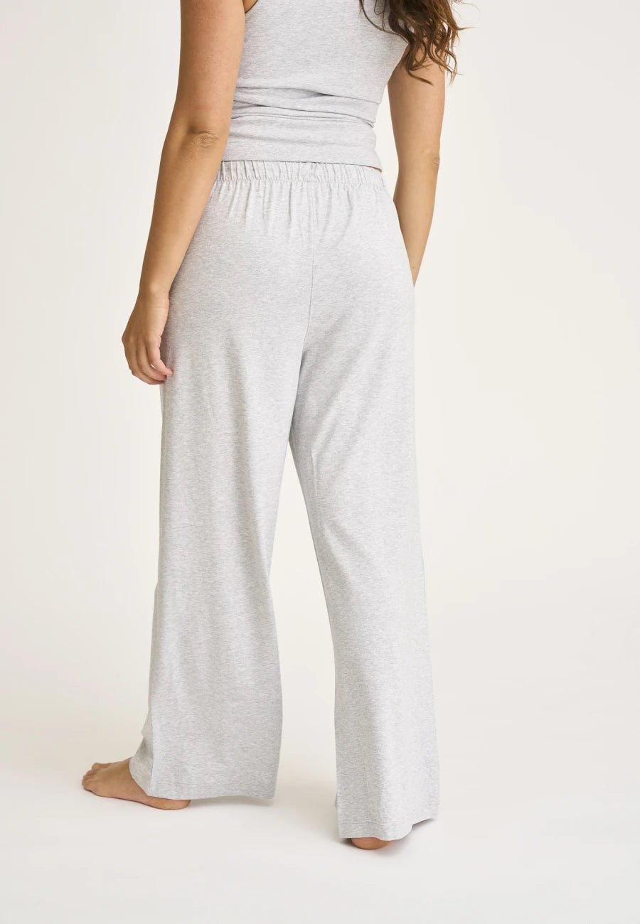 Person, der står barfodet i JBS of Denmark DK Pant Lysegrå, en lysegrå ærmeløs top, set bagfra.