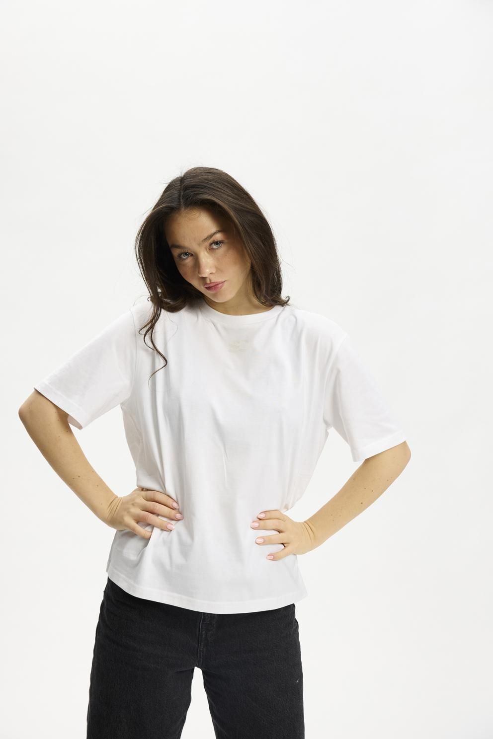 Modellen har en Kopenhaken Kenai Lady Hvid T-shirt på og står med hænderne i siden foran en ensfarvet hvid baggrund.
