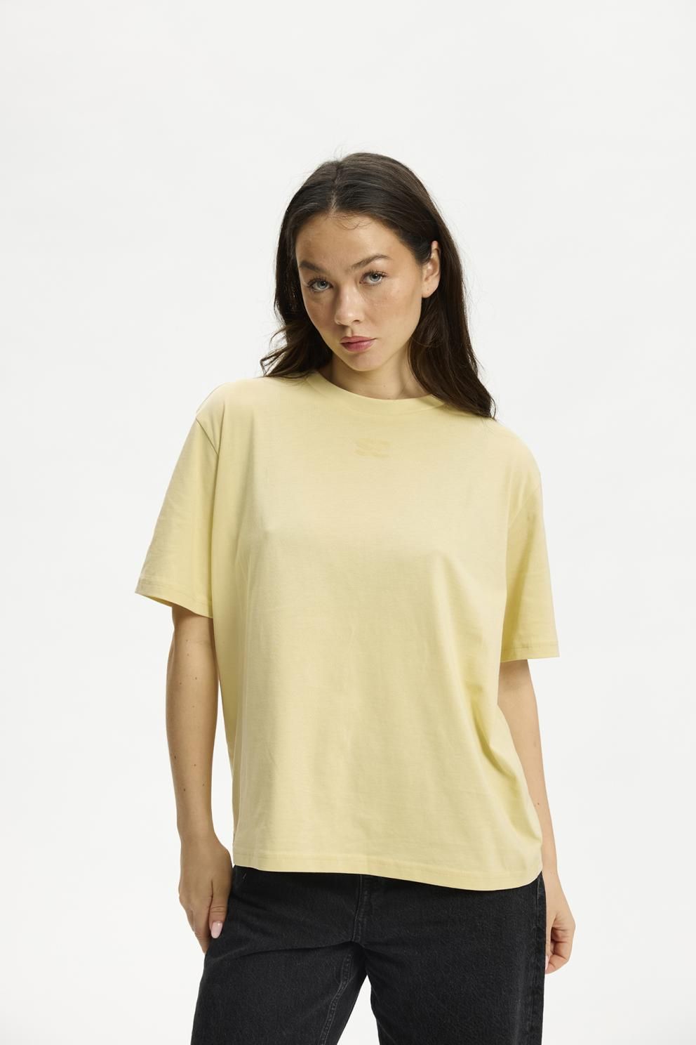 Kenai Lady har en ensfarvet gul Kopenhaken-T-shirt 153982 og sorte bukser på og står foran en hvid baggrund.