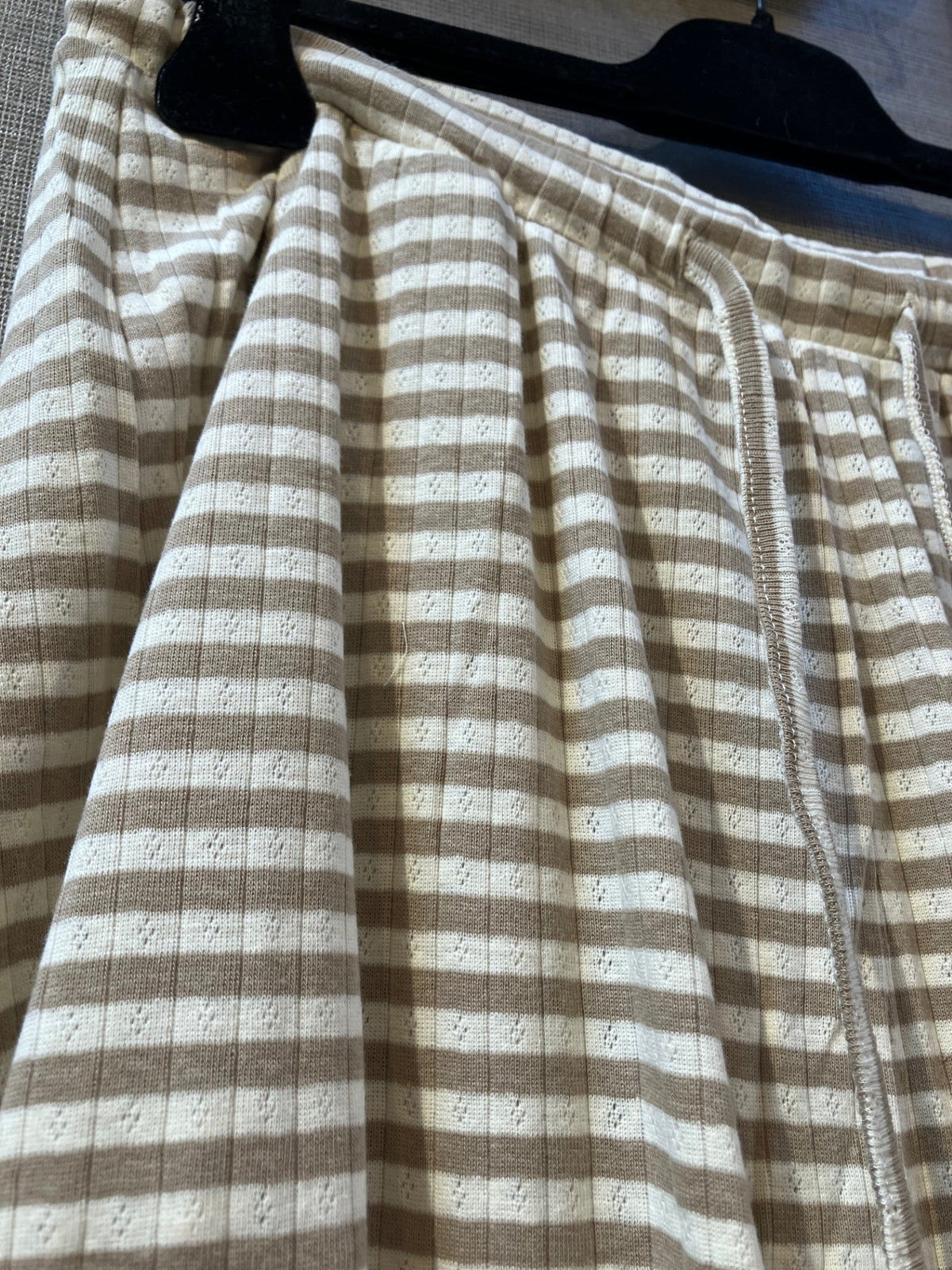 Nærbillede af Kopenhaken Soft Stripe Lysebrun-hjemmebukser med elastisk talje, hængende på en sort bøjle.