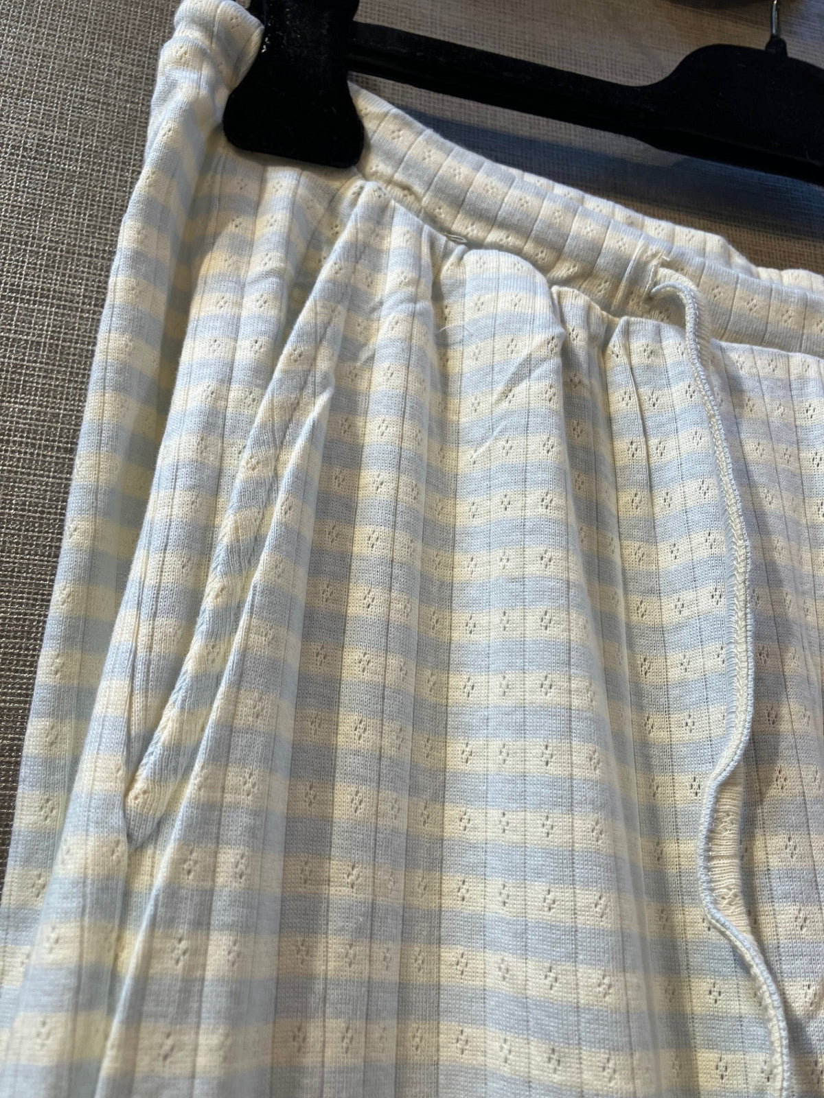 Nærbillede af Kopenhaken Soft Stripe Lyseblå loungebukser med snøre og lomme, hængende på en sort bøjle.