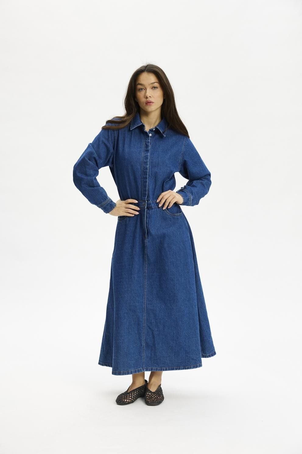 Kvinde i en Kopenhaken Osaka-denimkjole 154655 og sorte sko, stående foran en hvid baggrund.