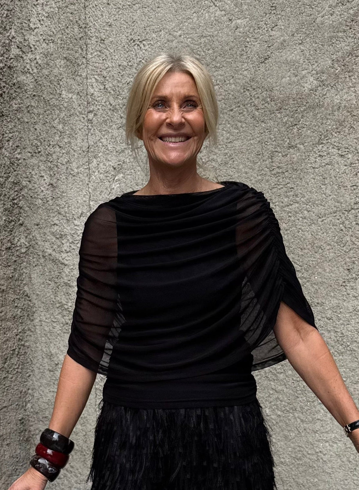 En smilende ældre kvinde i en Luxzuz - Queenie Sort-bluse, pyntet med armbånd, der udstråler en ubesværet stil.