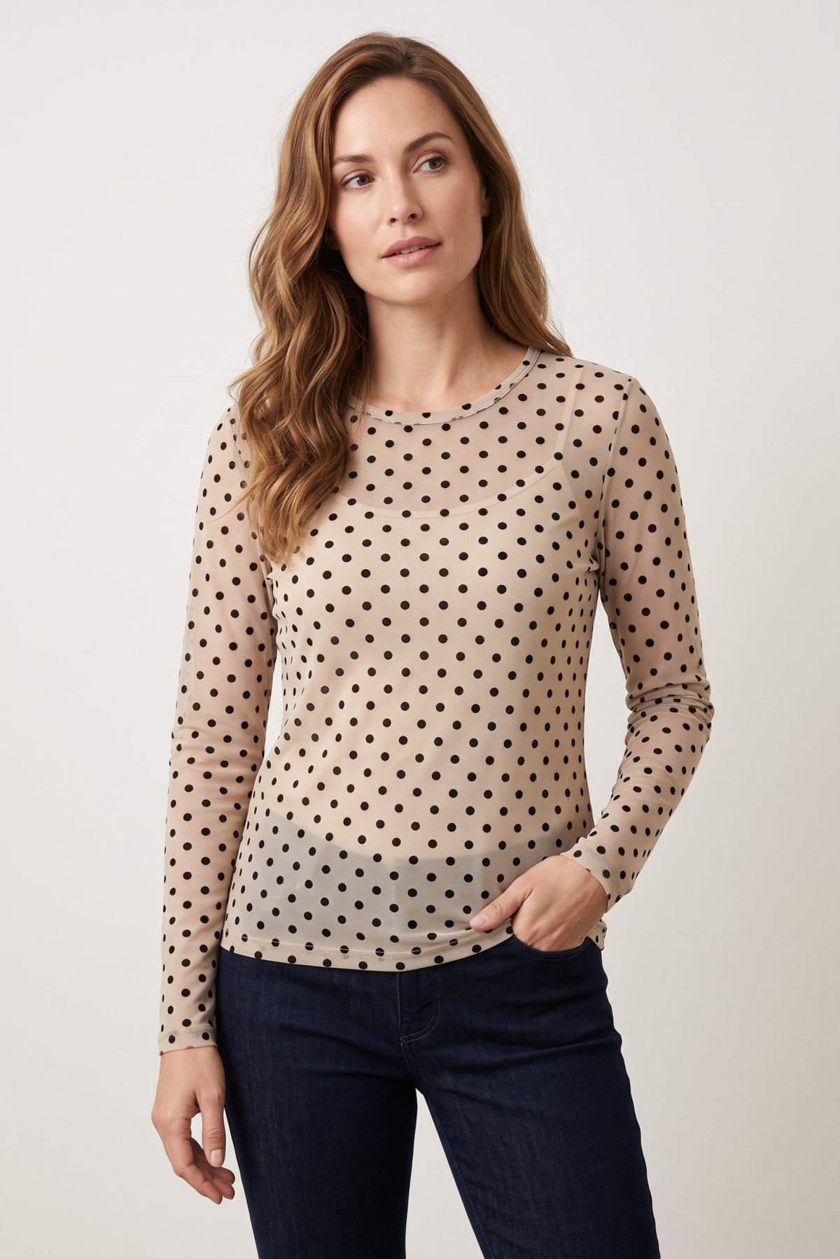 En kvinde har på sig model 156327 | Luxzuz – Dot Mesh: En offwhite langærmet mesh-top med sorte prikker og mørkeblå jeans.