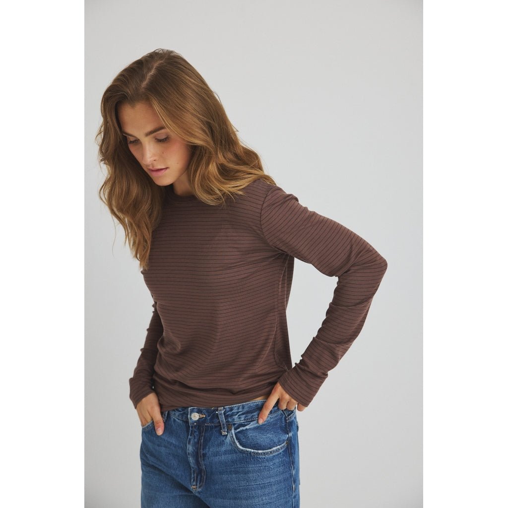Kvinde iført en brun 156422 | Luxzuz - Segberg Kakao langærmet T-shirt med tynde vandrette striber og blå jeans.