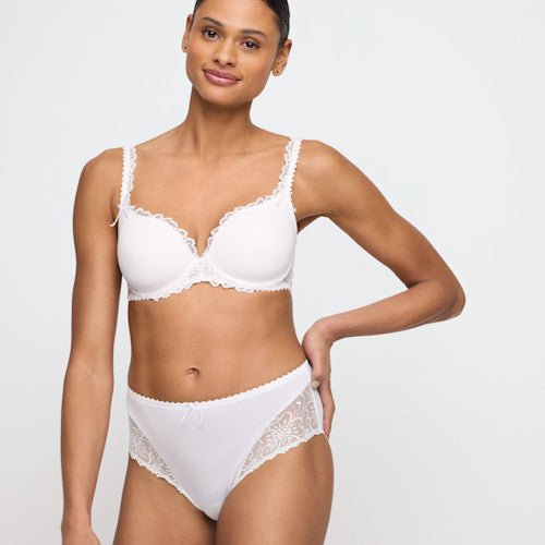 En kvinde iført en Marie Jo Jane Natural Off-white-bh og 130001-maxitrusse, der smiler let foran en ensfarvet baggrund.