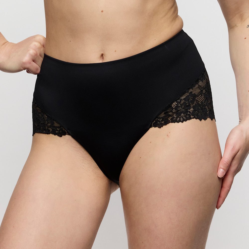 Model iført Marie Jo Soft Studio Black Sort maxi-trusse, med hænderne på hofterne, der poserer foran en ensfarvet baggrund.