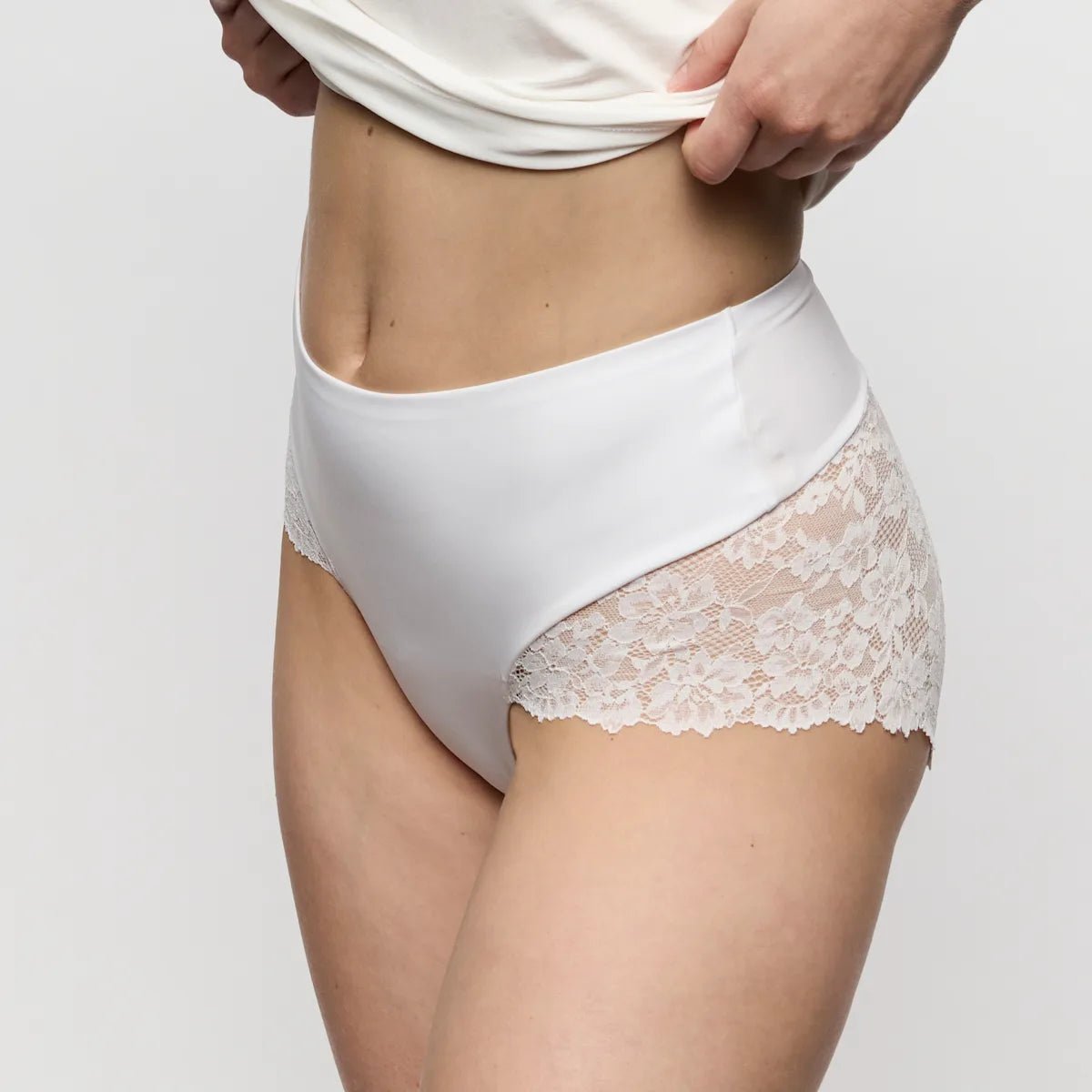 Model iført Marie Jo Soft Studio-trusser i offwhite og en hvid top, der går fra midt på brystet til låret, på en ensfarvet baggrund.