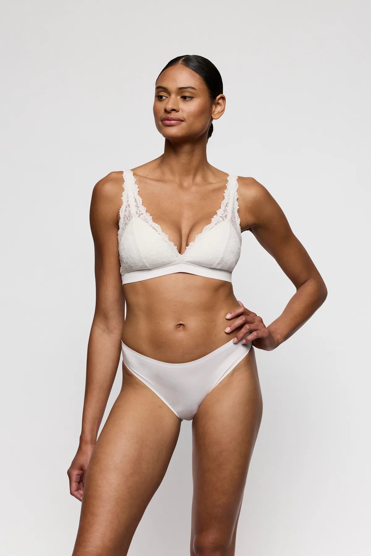 En kvinde står foran en ensfarvet baggrund iført en bralette fra Marie Jo – Soft Studio Off White – og Tai-trusser med sømløse kanter.