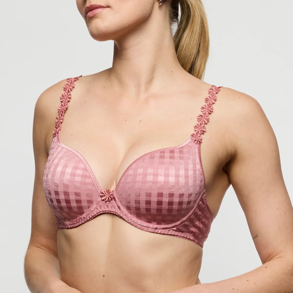 En kvinde bærer en Marie Jo - Avero 154398-bh i farven »Ballet pink Gammelrosa« med blomstermønstrede stropper og poserer foran en ensfarvet baggrund.