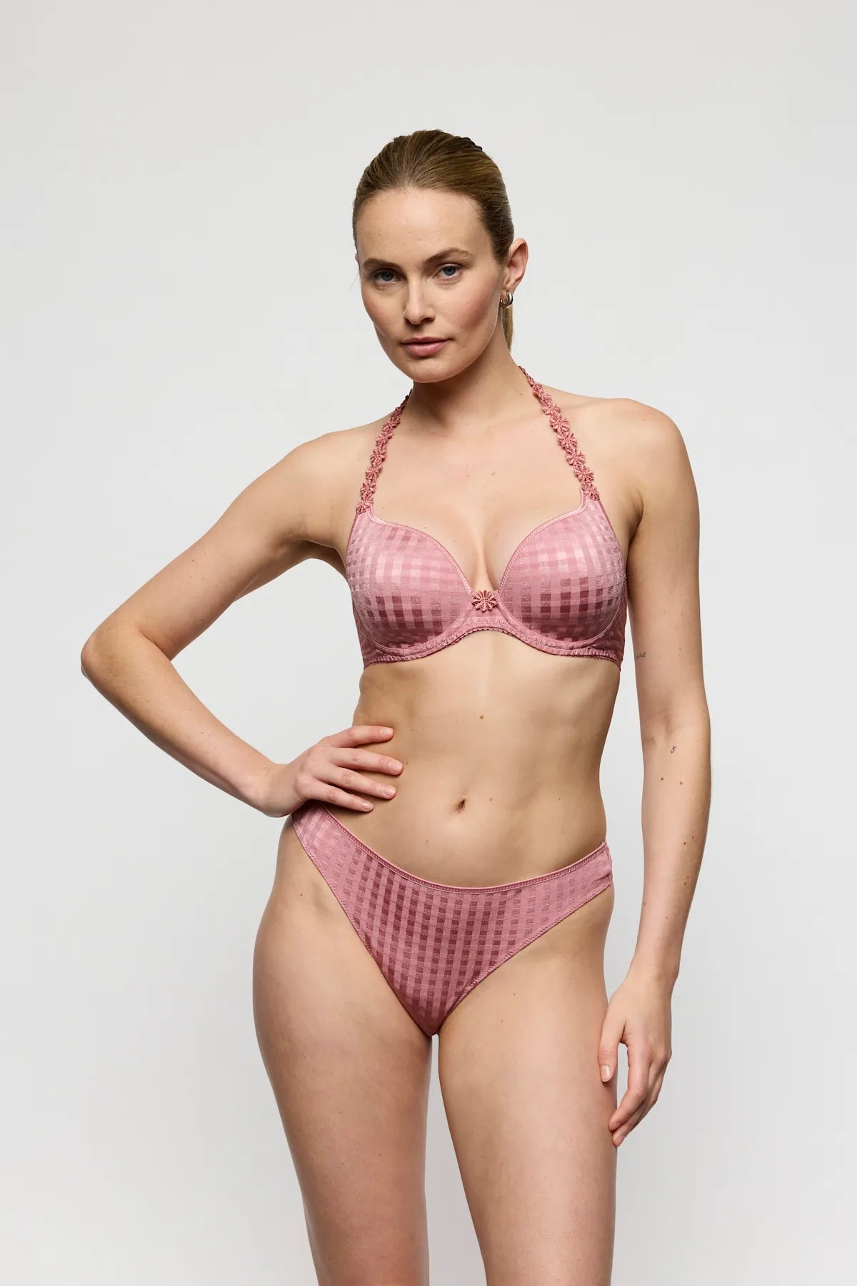 En model iført en lyserød bh og trusser fra Marie Jo Avero Ballet poserer foran en ensfarvet lysegrå baggrund.